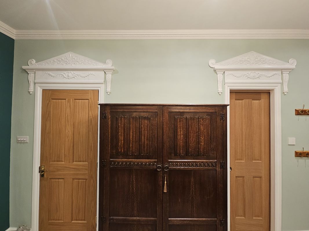A pair of classical door frames, featuring carved corbels, frieze and pointed pediment in matching style. Undercoat and finished in white interior paint.